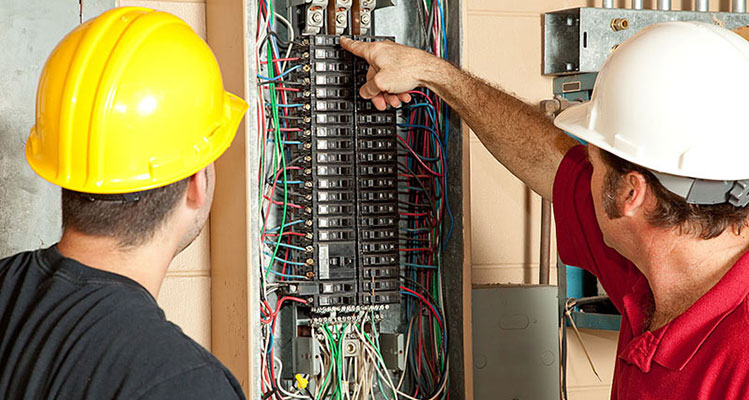 two electricians looking over a breaker box